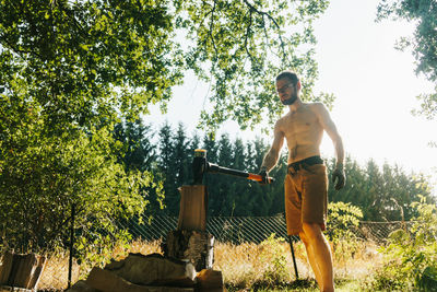 Full length of shirtless man standing against trees