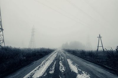 Road by electricity pylon against sky during winter