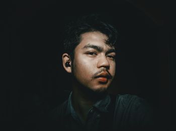 Portrait of young man standing against black background