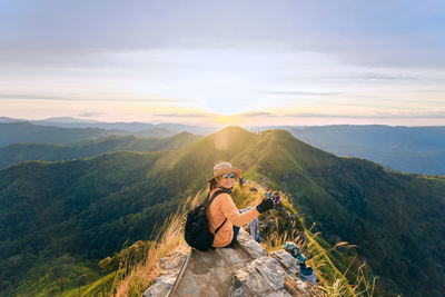 Woman sitting on mountain against sky