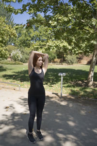 Fitness young redhead woman doing stretching exercise outdoors in public park.