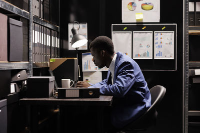 Rear view of man using laptop while standing in office