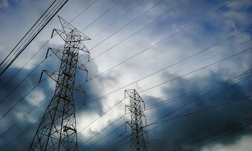 Low angle view of electricity pylon against cloudy sky