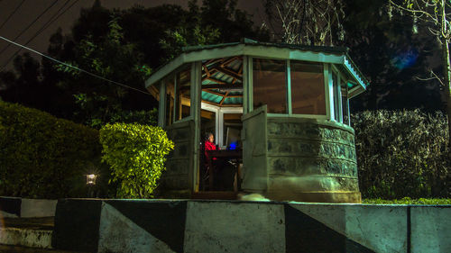 Woman using computer while sitting in gazebo at night