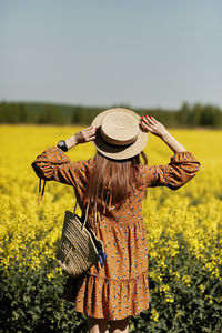 Rear view. beautiful young woman in a dress holding a hat and walking in a rapeseed field for summer