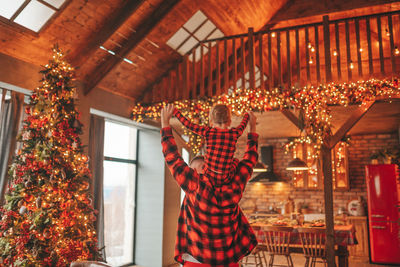 Candid authentic happy dad and son in red plaid pajamas fooling around at wood lodge xmas decorated