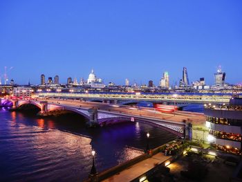 Light trail on arch bridge over thames river against clear blue sky at dusk