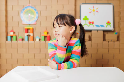 Portrait of young girl sitting on chair against carton block wall background 