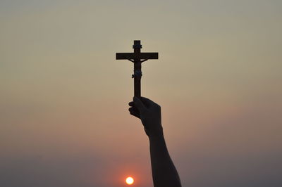 Silhouette person on cross against sky during sunset