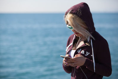 Young woman using mobile phone against sea