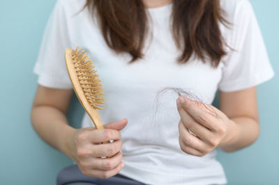 Midsection of woman holding brush with hair against blue background