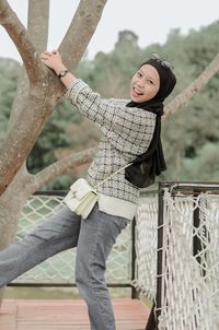 Portrait of young woman standing against fence