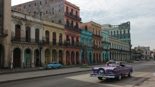 Cars on road by buildings against sky in city