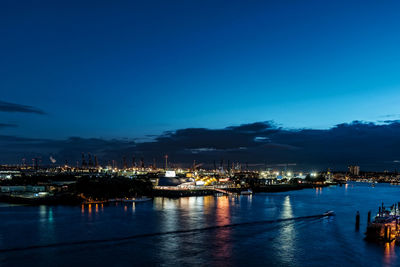 Illuminated city by sea against blue sky at dusk