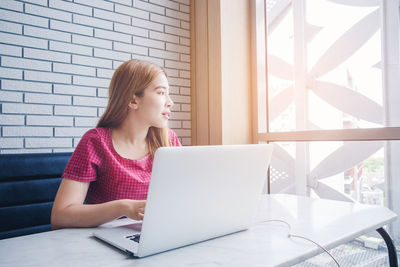 Young businesswoman looking away while using laptop at table in cafe