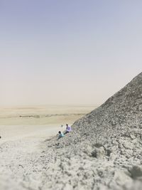 Father and son sitting on rocks against clear sky