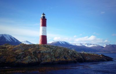 Lighthouse by sea and mountain against sky