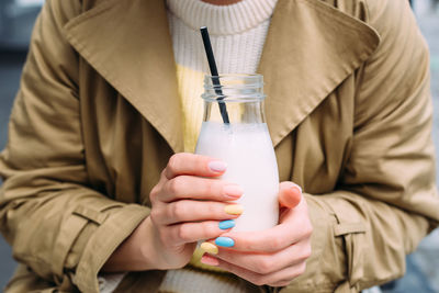 A young woman drinks a milkshake outdoors from a stylish glass jar with a straw