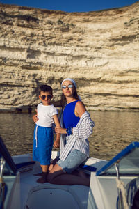 Woman and a boy  in sunglasses are sitting on yacht near rocks in  sea in summer