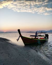 Boat moored at beach against sky during sunset