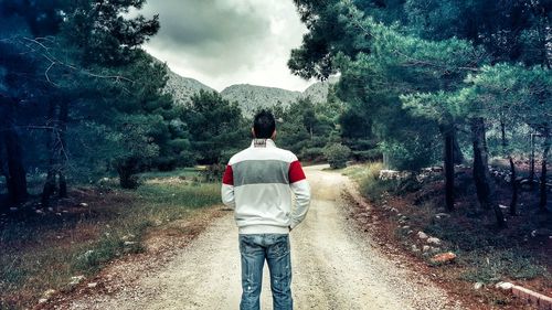 Rear view of man standing on dirt road at field