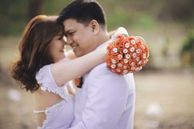 Side view of bride holding bouquet embracing groom on field