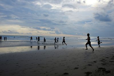 People playing on beach against sky during sunset