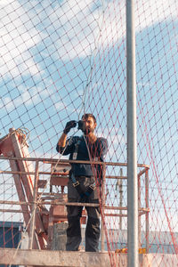 Man working on fence against sky