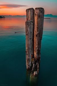 Wooden post in sea against sky during sunset