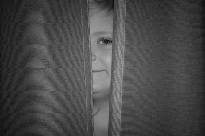 Close-up portrait of girl looking through curtain