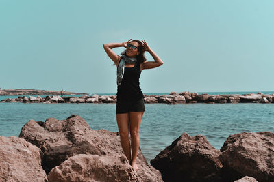 Woman standing on rock by sea against sky