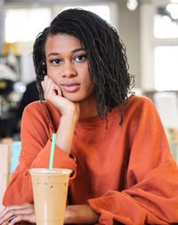 Portrait of young woman sitting with drink at cafe