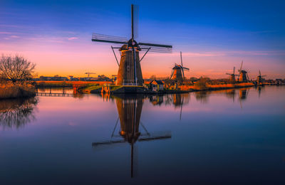 Reflection of traditional windmill on lake against sky during sunset