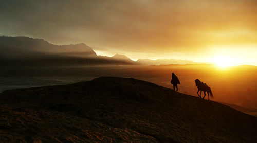 Silhouette people riding horse on mountain against sunset sky