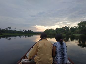 Rear view of friends standing in lake against sky during sunset