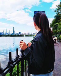 Rear view of woman standing by railing against sky