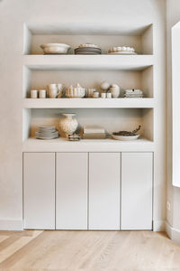 Elegant ceramic plates cups and vases arranged on built in shelves in minimalist style apartment with wooden parquet floor in daylight