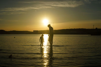 Silhouette people on water against orange sky