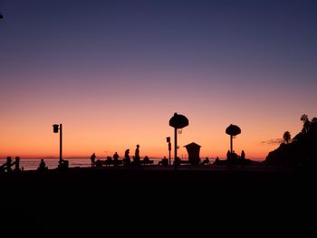 Silhouette people on street against clear sky during sunset