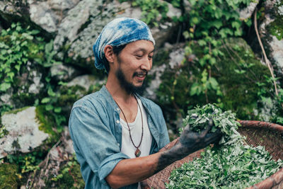 Smiling man holding basket with plants while standing against rocks