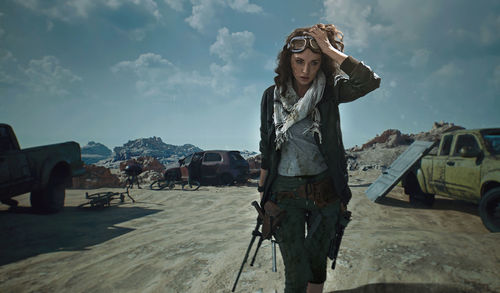 Woman holding weapon while walking on desert against sky