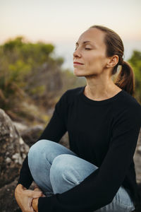 Woman with eyes closed sitting on rock
