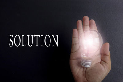 Close-up of hand holding light bulb over black background