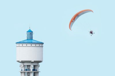 Person paragliding by tower against clear sky