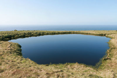 Scenic view of pond in front of sea against clear blue sky