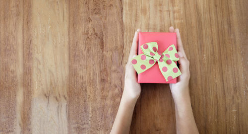 Cropped hands of woman holding gift on table at home