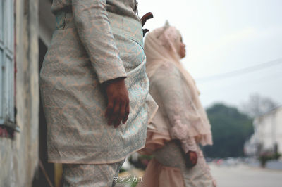 Midsection of man holding camera while standing against sky