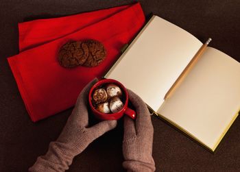 High angle view of hands holding hot chocolate by book on table