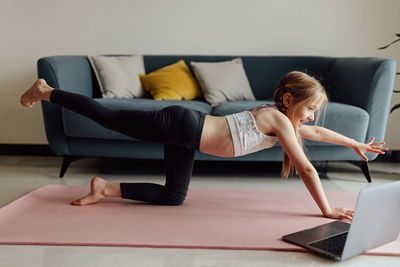 Full length of woman exercising on sofa at home