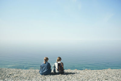 Rear view of friends sitting on sea against sky